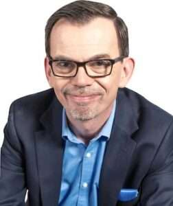 photo of Jason Reid, invisible disability expert: a smiling, white gen-x man with glasses in a blue suit.